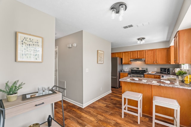 kitchen featuring kitchen peninsula, light stone countertops, dark wood-type flooring, appliances with stainless steel finishes, and a breakfast bar area