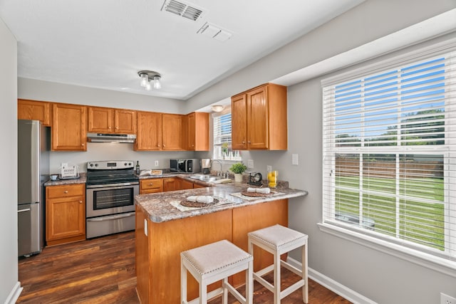 kitchen featuring kitchen peninsula, dark wood-type flooring, sink, stainless steel appliances, and a breakfast bar area