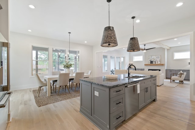 kitchen with sink, dark stone counters, dishwasher, light hardwood / wood-style floors, and decorative light fixtures