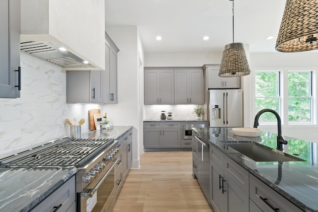 kitchen featuring pendant lighting, dark stone countertops, high end appliances, premium range hood, and tasteful backsplash