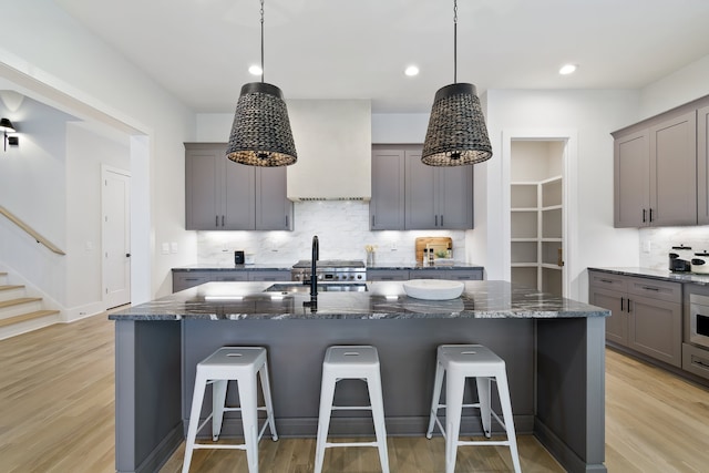 kitchen with an island with sink, dark stone counters, a breakfast bar, tasteful backsplash, and light wood-type flooring