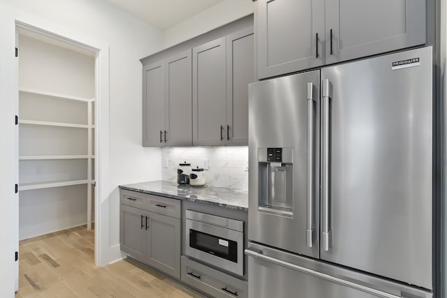 kitchen with appliances with stainless steel finishes, tasteful backsplash, light stone counters, gray cabinetry, and light hardwood / wood-style floors