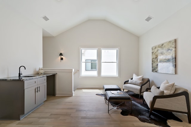 living area with lofted ceiling, sink, and light hardwood / wood-style flooring