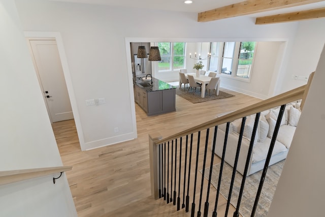 stairs featuring an inviting chandelier, beamed ceiling, and light wood-type flooring