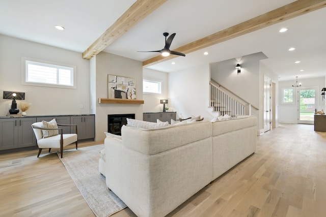 living room featuring beam ceiling, light hardwood / wood-style floors, and ceiling fan with notable chandelier