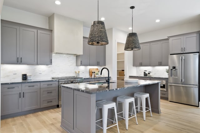 kitchen featuring light hardwood / wood-style floors, tasteful backsplash, a center island with sink, dark stone countertops, and high end appliances