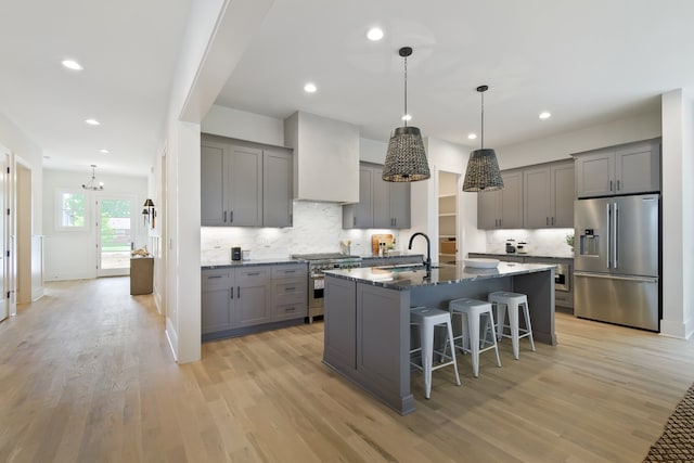 kitchen with a kitchen bar, an island with sink, light wood-type flooring, high end appliances, and hanging light fixtures