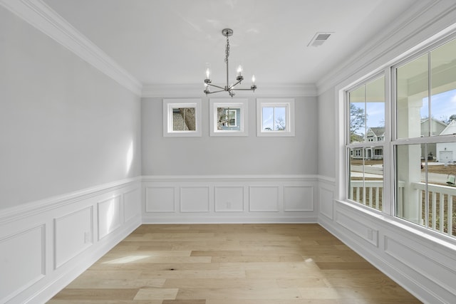 spare room with a chandelier, ornamental molding, and light hardwood / wood-style flooring