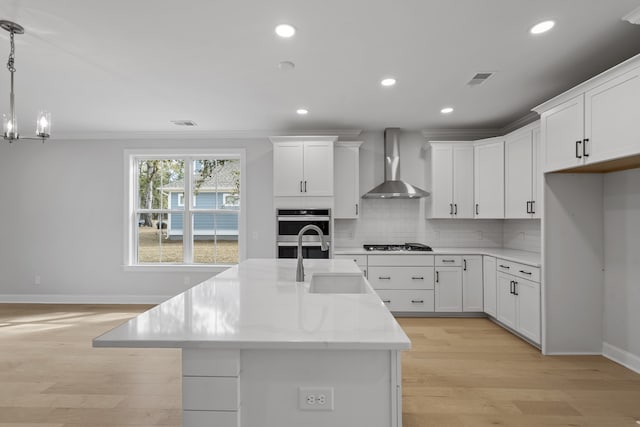 kitchen with decorative light fixtures, sink, light wood-type flooring, tasteful backsplash, and wall chimney exhaust hood