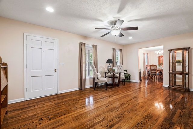 sitting room featuring a textured ceiling, ceiling fan with notable chandelier, and dark wood-type flooring