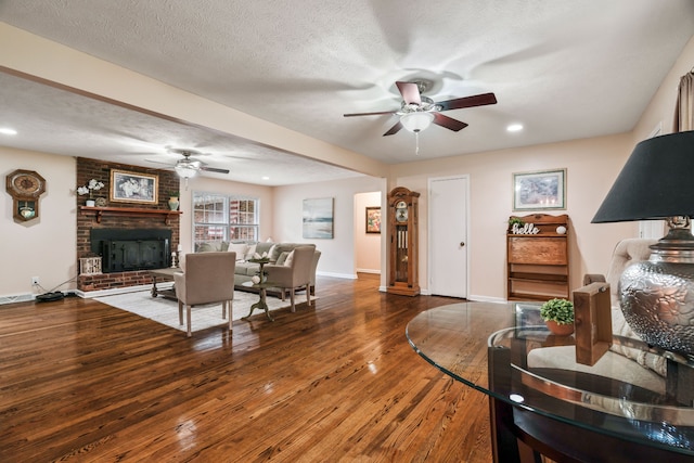 living room featuring ceiling fan, a textured ceiling, dark wood-type flooring, and a brick fireplace