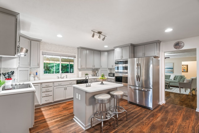 kitchen with appliances with stainless steel finishes, a center island, dark wood-type flooring, backsplash, and a kitchen bar