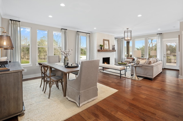 dining area with a stone fireplace, dark hardwood / wood-style floors, a chandelier, and crown molding