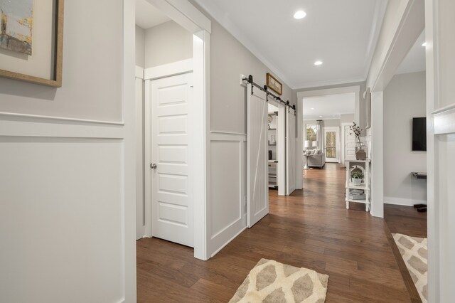 corridor featuring a barn door, ornamental molding, and dark hardwood / wood-style flooring