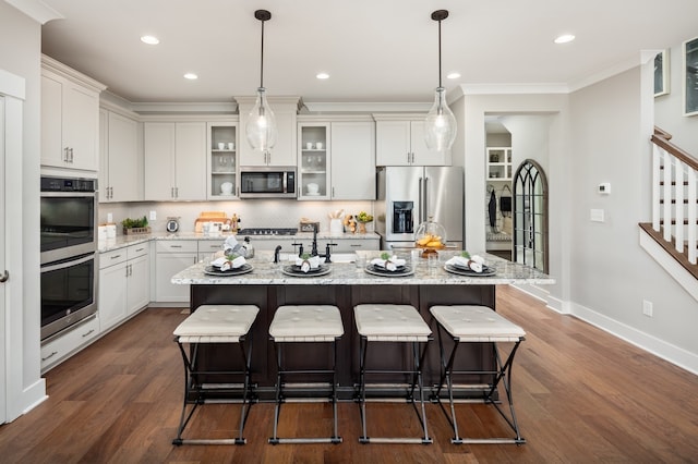 kitchen featuring dark hardwood / wood-style floors, an island with sink, hanging light fixtures, appliances with stainless steel finishes, and tasteful backsplash