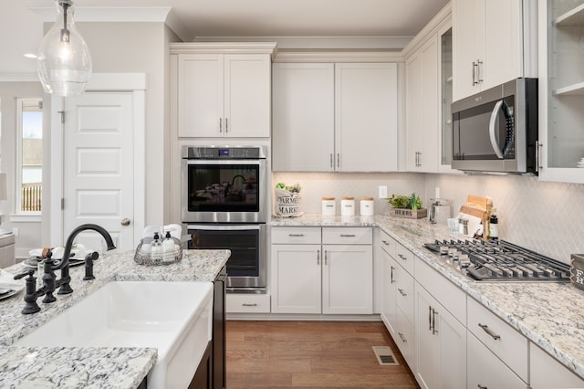 kitchen with appliances with stainless steel finishes, light hardwood / wood-style floors, tasteful backsplash, sink, and hanging light fixtures