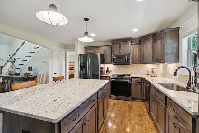 kitchen with hanging light fixtures, stainless steel appliances, sink, and light wood-type flooring