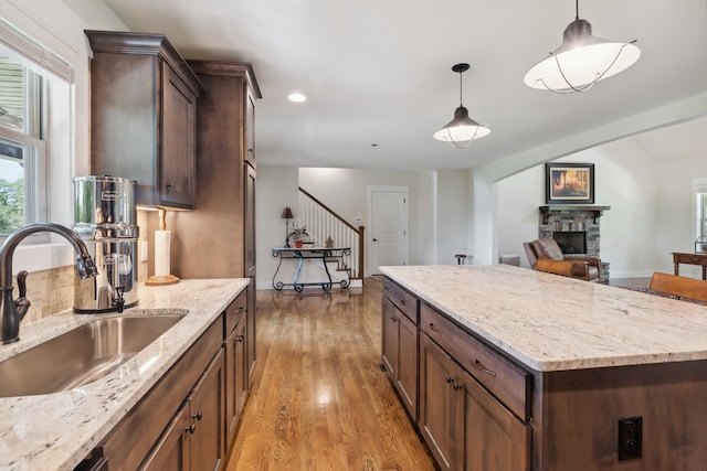 kitchen featuring hanging light fixtures, sink, a stone fireplace, light hardwood / wood-style flooring, and light stone countertops