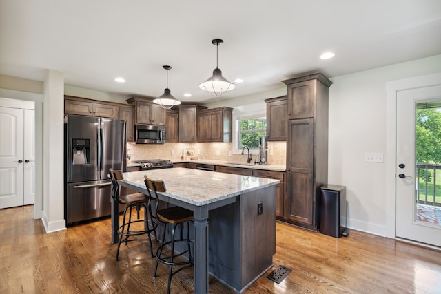 kitchen with light hardwood / wood-style floors, a kitchen island, light stone countertops, appliances with stainless steel finishes, and backsplash