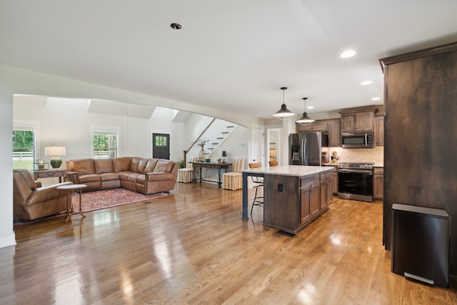 kitchen with backsplash, light wood-type flooring, stainless steel appliances, a kitchen island, and a breakfast bar area