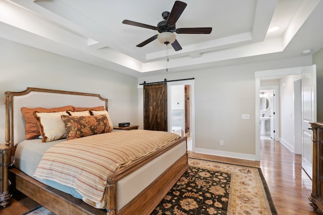 bedroom featuring a raised ceiling, a barn door, ceiling fan, and light hardwood / wood-style flooring