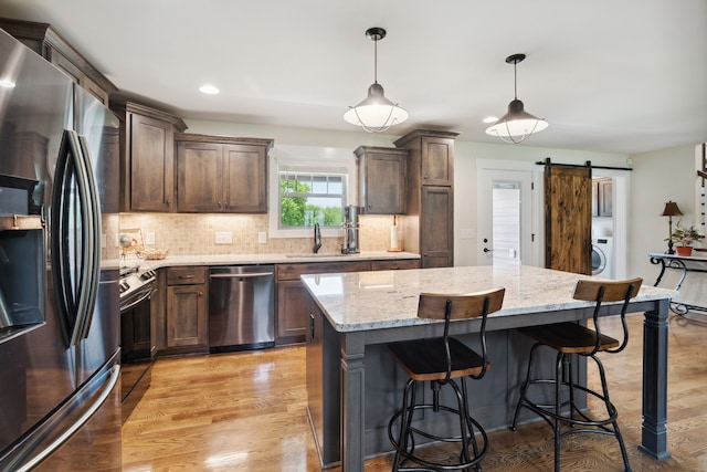 kitchen with appliances with stainless steel finishes, tasteful backsplash, decorative light fixtures, a barn door, and light hardwood / wood-style flooring