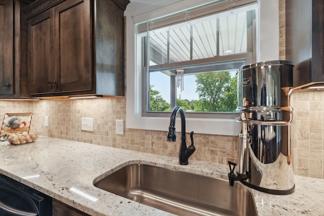 kitchen with dark brown cabinetry, sink, light stone counters, and tasteful backsplash