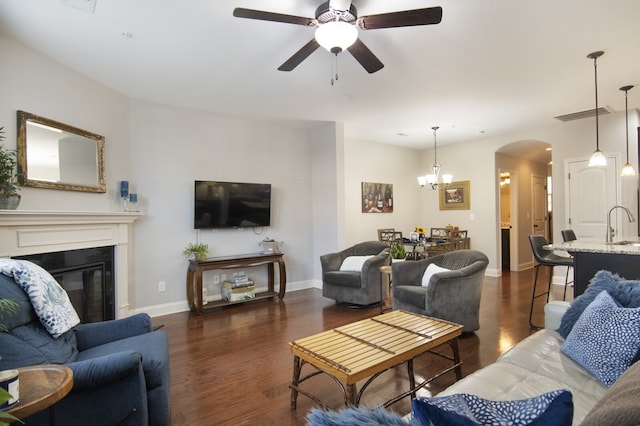 living room with dark hardwood / wood-style flooring, ceiling fan with notable chandelier, and sink