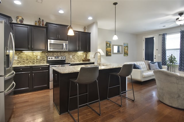 kitchen featuring dark hardwood / wood-style flooring, backsplash, stainless steel appliances, ceiling fan, and a kitchen breakfast bar