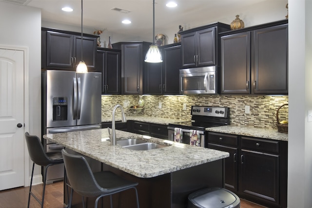 kitchen with an island with sink, pendant lighting, sink, backsplash, and stainless steel appliances