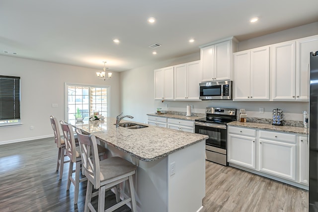 kitchen featuring white cabinetry, stainless steel appliances, a notable chandelier, light wood-type flooring, and sink