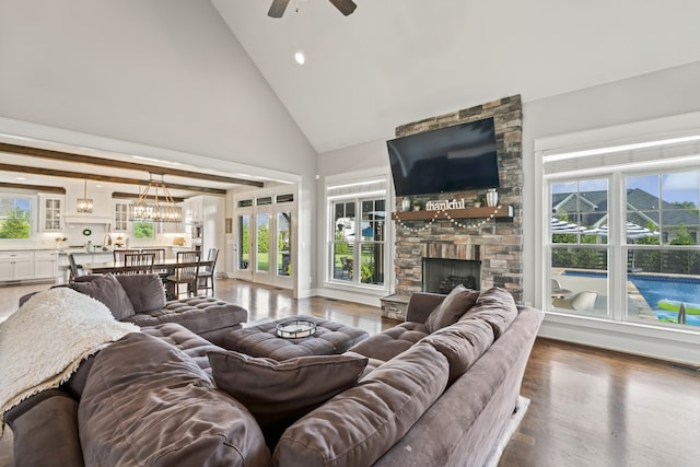 living room featuring dark wood-type flooring, beamed ceiling, high vaulted ceiling, a fireplace, and ceiling fan with notable chandelier