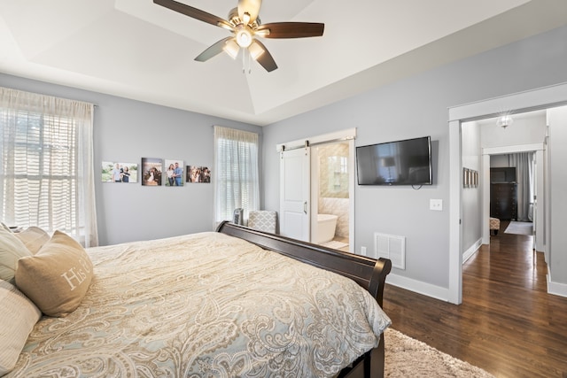 bedroom featuring dark hardwood / wood-style flooring, ensuite bathroom, a barn door, and a tray ceiling