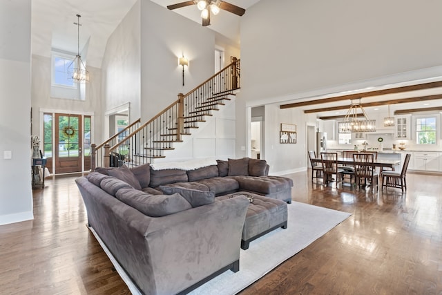 living room featuring light hardwood / wood-style floors, ceiling fan with notable chandelier, a towering ceiling, and beamed ceiling