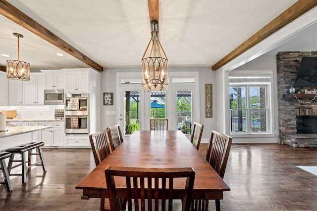 dining room with beamed ceiling, a stone fireplace, dark wood-type flooring, and an inviting chandelier