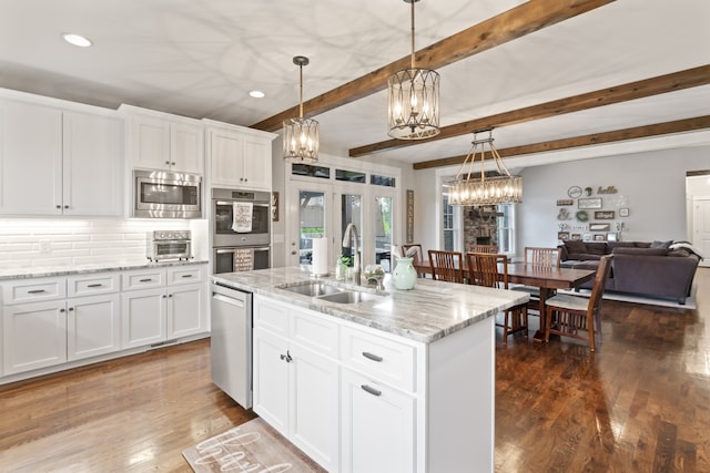 kitchen with beam ceiling, a center island with sink, appliances with stainless steel finishes, white cabinetry, and sink