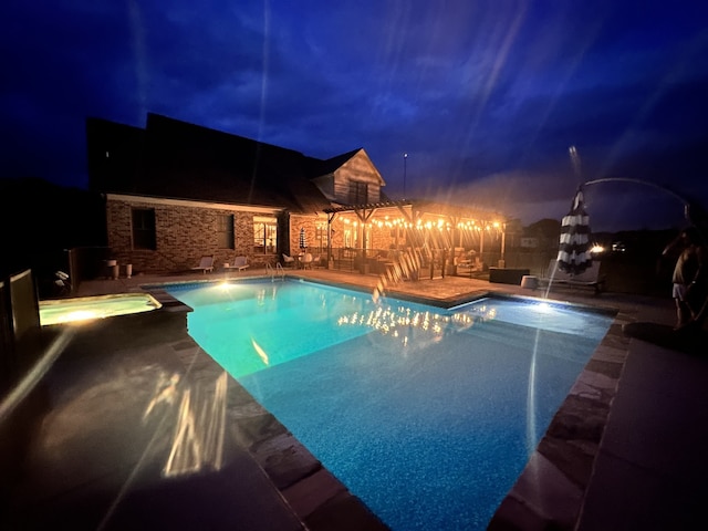 pool at night with a patio area and an in ground hot tub