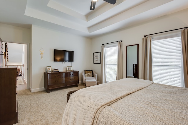 bedroom with light carpet, a raised ceiling, and ceiling fan