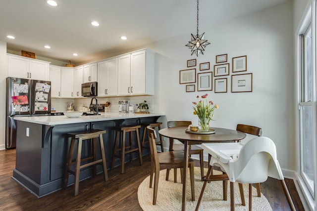 kitchen with a breakfast bar area, stainless steel appliances, dark wood-type flooring, decorative light fixtures, and white cabinetry