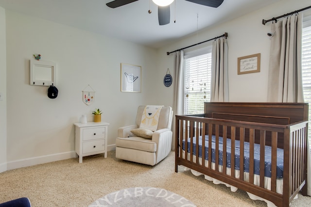 bedroom with ceiling fan, light colored carpet, and a nursery area