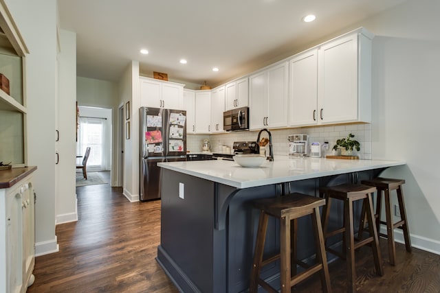 kitchen with a breakfast bar area, stainless steel appliances, backsplash, dark hardwood / wood-style flooring, and white cabinetry