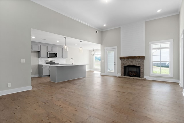 kitchen featuring backsplash, a kitchen island with sink, a brick fireplace, light wood-type flooring, and pendant lighting