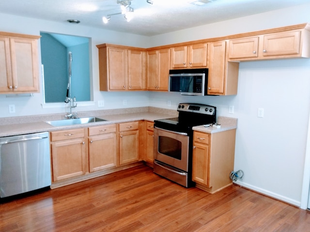 kitchen with appliances with stainless steel finishes, sink, and light hardwood / wood-style flooring