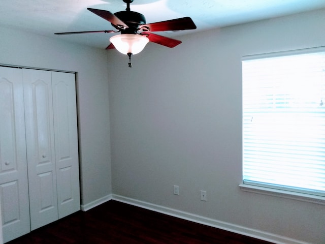 unfurnished bedroom featuring ceiling fan, dark wood-type flooring, multiple windows, and a closet