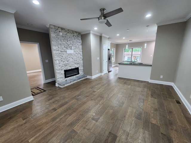 unfurnished living room featuring ceiling fan, ornamental molding, dark wood-type flooring, a stone fireplace, and sink