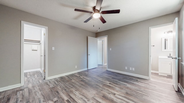 unfurnished bedroom featuring a closet, a walk in closet, ceiling fan, and hardwood / wood-style flooring