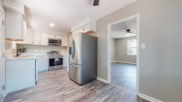 kitchen with white cabinets, stainless steel appliances, light hardwood / wood-style flooring, ceiling fan, and sink