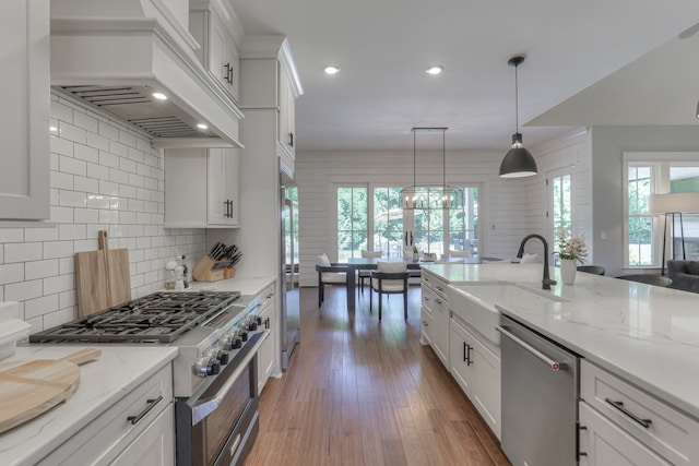 kitchen featuring high end appliances, plenty of natural light, decorative light fixtures, and premium range hood