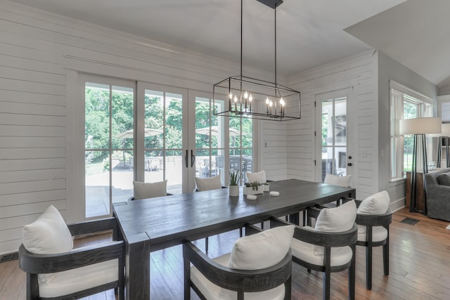 dining area featuring wooden walls, hardwood / wood-style flooring, a chandelier, and a healthy amount of sunlight