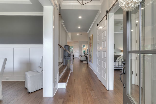 corridor with a barn door, a notable chandelier, crown molding, and wood-type flooring